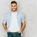 Portrait of handsome smiling hipster lumbersexual businessman model wearing casual shirt clothes. Fashion stylish man posing against gray wall