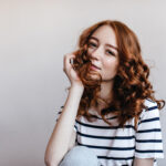 Elegant ginger woman touching her hair with smile. Studio photo of dreamy european girl with beautiful eyes.
